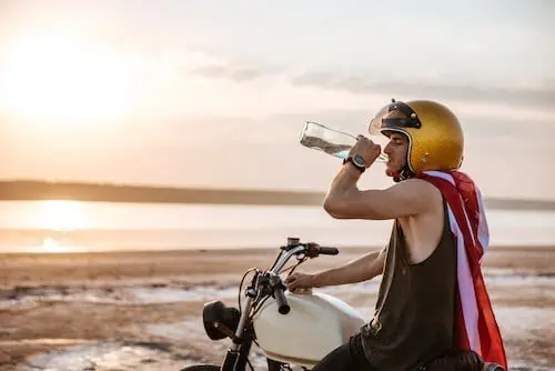 rider drinks water under hot sun while sitting on motorcycle